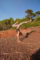 Blonde woman practicing a variation of handstand yoga pose in the middle of the forest