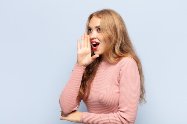 Vista di profilo della donna bionda, che sembra felice ed eccitata, gridando e chiamando per copiare lo spazio sul lato