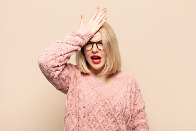 blonde woman raising palm to forehead thinking oops, after making a stupid mistake or remembering, feeling dumb