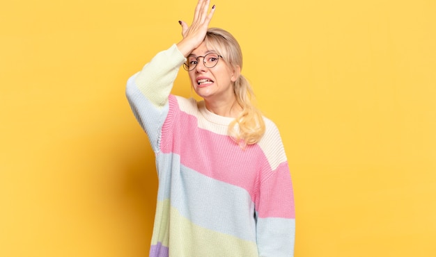 Blonde woman raising palm to forehead thinking oops, after making a stupid mistake or remembering