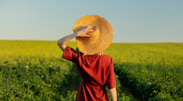 Блондинка в красном платье и соломенной шляпе в поле рапса