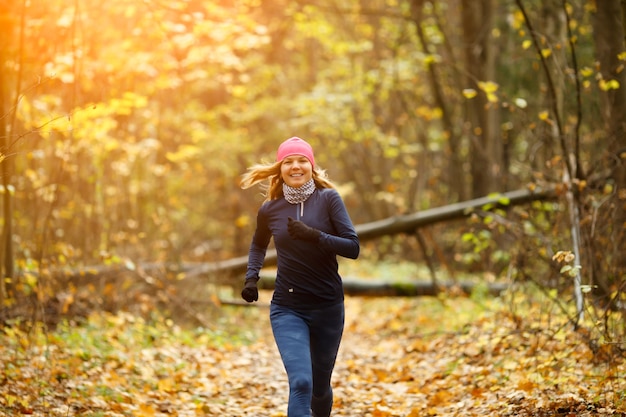 秋の森で朝走っている金髪の女性