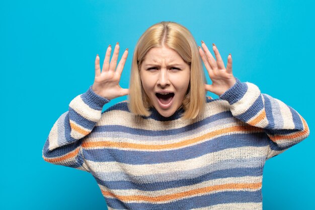 Blonde woman screaming in panic or anger, shocked, terrified or furious, with hands next to head