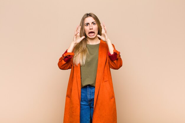 Blonde woman screaming with hands up in the air, feeling furious, frustrated, stressed and upset