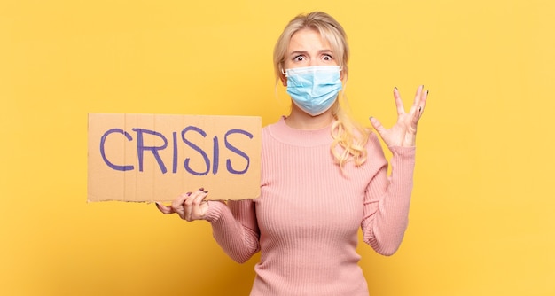 Blonde woman screaming with hands up in the air, feeling furious, frustrated, stressed and upset