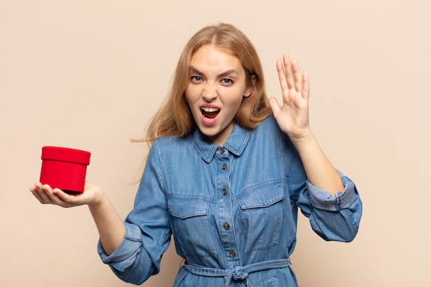 Blonde woman screaming with hands up in the air, feeling furious, frustrated, stressed and upset