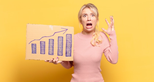 Photo blonde woman screaming with hands up in the air, feeling furious, frustrated, stressed and upset