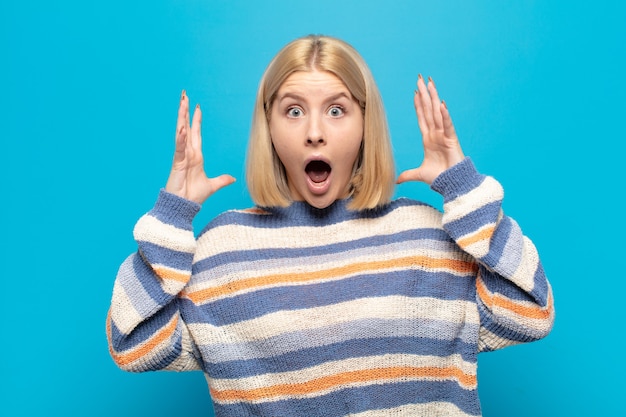 Blonde woman screaming with hands up in the air, feeling furious, frustrated, stressed and upset