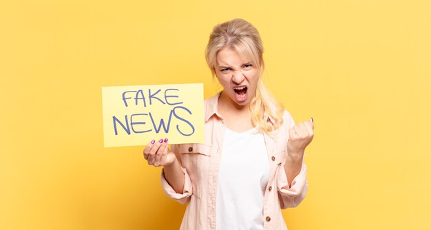 Blonde woman shouting aggressively with an angry expression or with fists clenched celebrating success