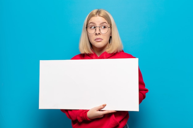 Photo blonde woman shrugging, feeling confused and uncertain, doubting with arms crossed and puzzled look