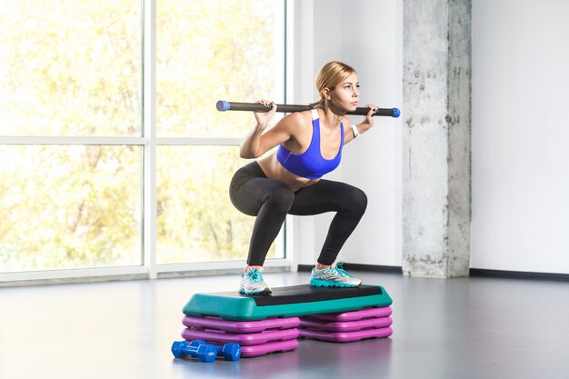 Blonde woman sit-ups, squad on step platform with barbell. Studio shot