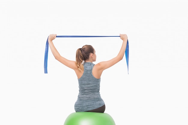 Blonde woman sitting on a fitness ball training with a resistance band