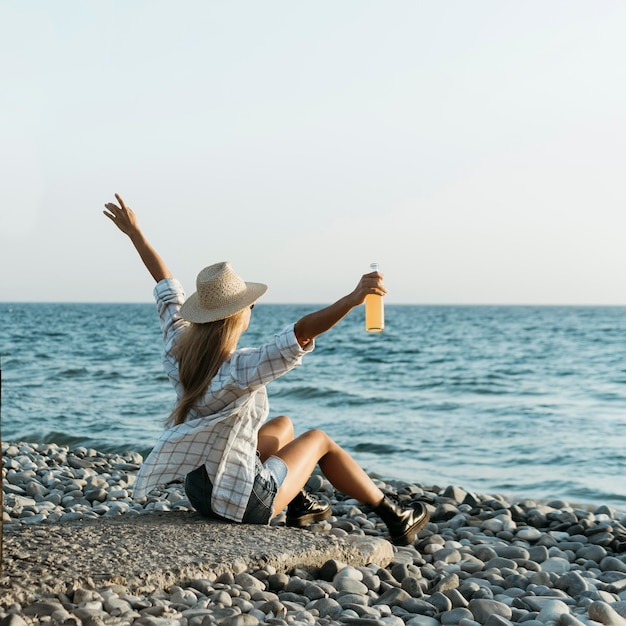 写真 海を見ているジュースと岩の上に座っているブロンドの女性