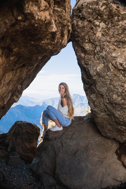 Blonde woman sitting on a rock with the amazing view of Roque Nublo in Gran Canaria