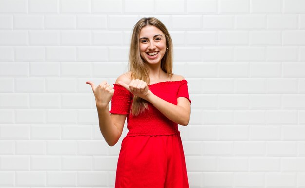 Blonde woman smiling cheerfully and casually pointing to copy space on the side, feeling happy and satisfied