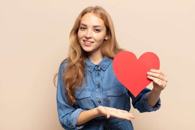 Donna bionda che sorride allegramente, sentendosi felice e mostrando un concetto nello spazio della copia con il palmo della mano