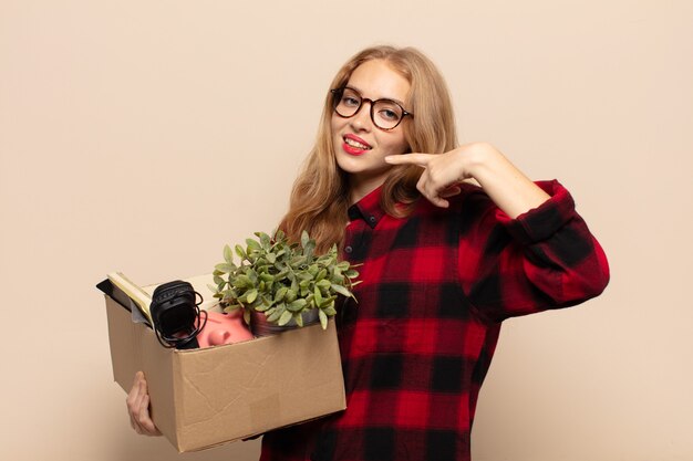 Blonde woman smiling confidently pointing to own broad smile, positive, relaxed, satisfied attitude