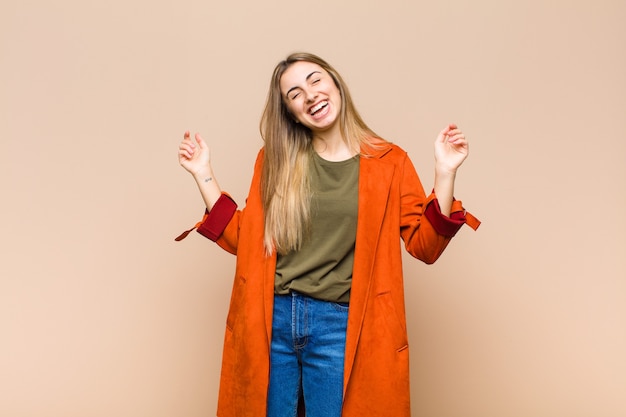 Blonde woman smiling, feeling carefree, relaxed and happy, dancing and listening to music, having fun at a party