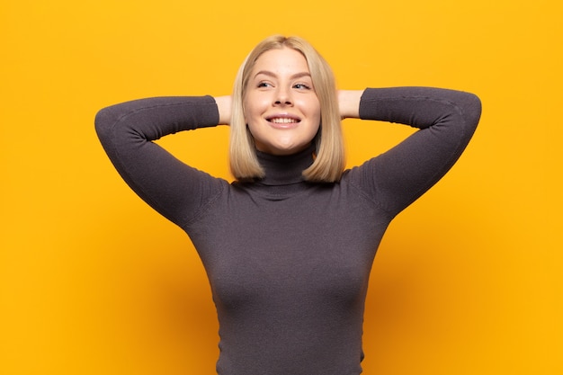 Blonde woman smiling and feeling relaxed, satisfied and carefree, laughing positively and chilling