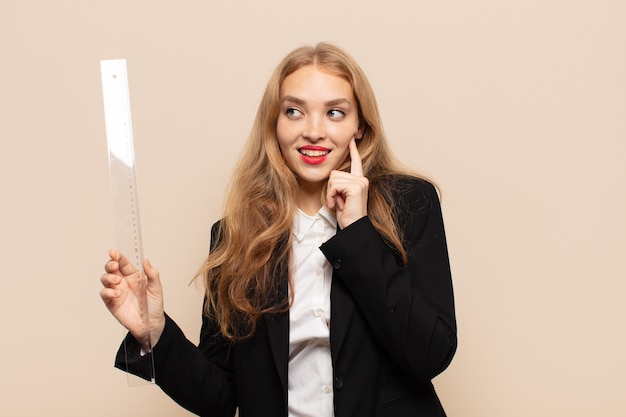 Blonde woman smiling happily and daydreaming or doubting, looking to the side