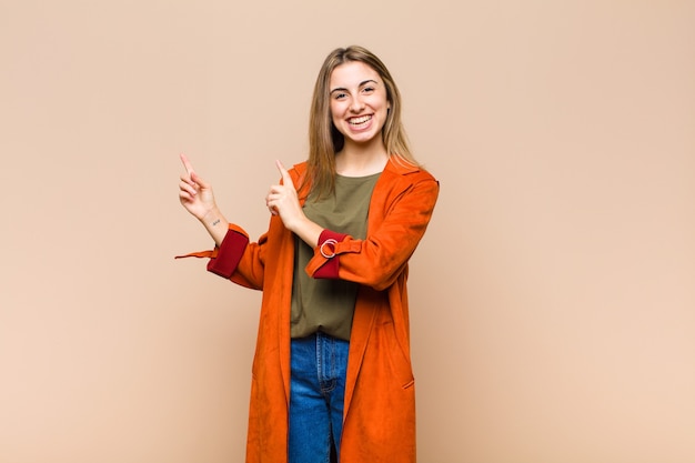 Blonde woman smiling happily and pointing to side and upwards with both hands showing object in copy space