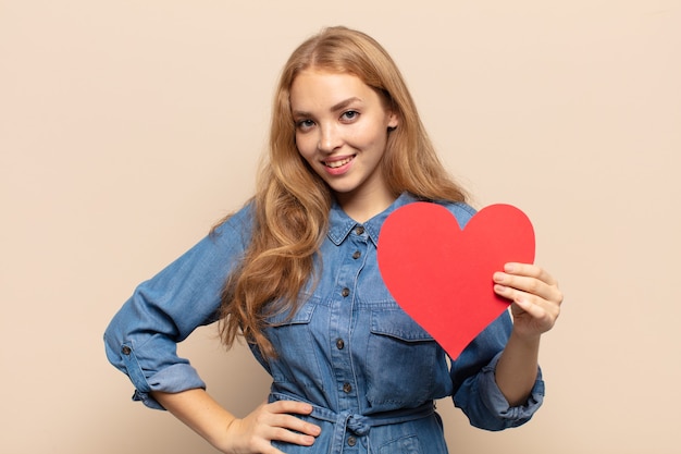 Blonde woman smiling happily with a hand on hip and confident, positive, proud and friendly attitude