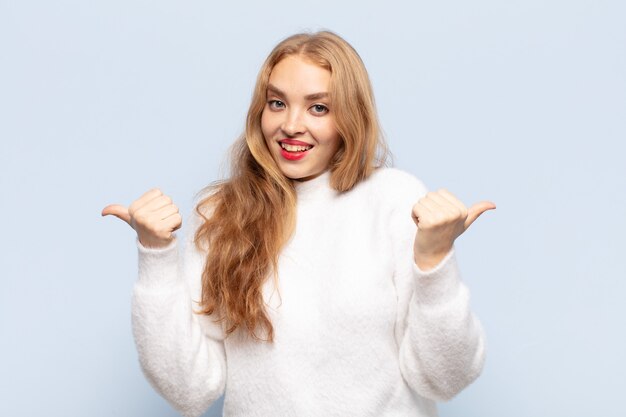 Blonde woman smiling joyfully and looking happy, feeling carefree and positive with both thumbs up