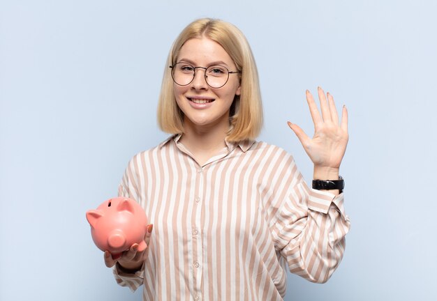 Donna bionda che sorride e sembra amichevole, mostrando il numero cinque o quinto con la mano in avanti, contando alla rovescia