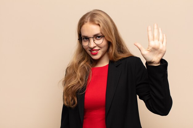 Donna bionda sorridente e dall'aspetto amichevole, che mostra il numero cinque o il quinto con la mano in avanti, conto alla rovescia