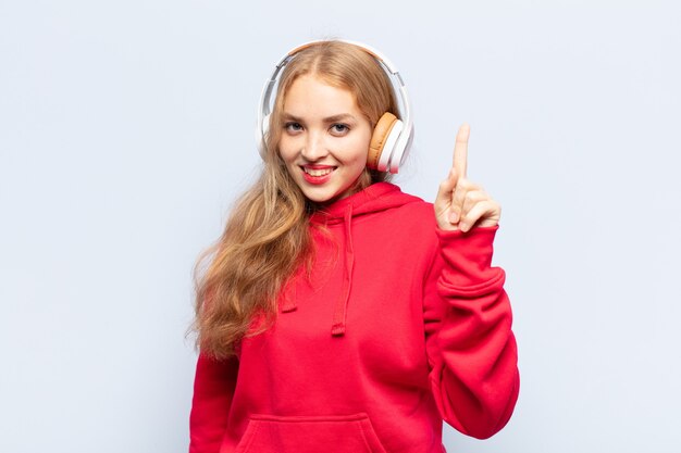 Blonde woman smiling and looking friendly, showing number one or first with hand