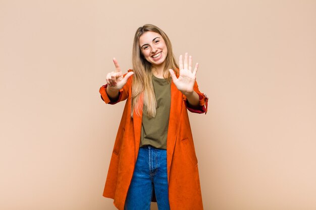 Blonde woman smiling and looking friendly, showing number seven or seventh with hand forward, counting down