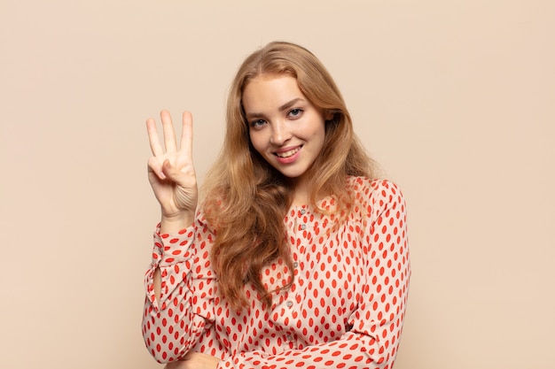 Blonde woman smiling and looking friendly, showing number three or third with hand forward, counting down