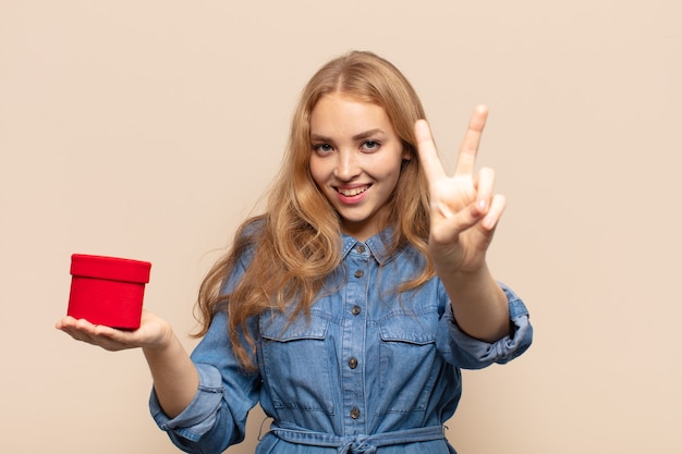 blonde woman smiling and looking happy, carefree and positive, gesturing victory or peace with one hand