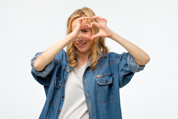 Blonde woman smiling in love showing heart symbol and shape with hands