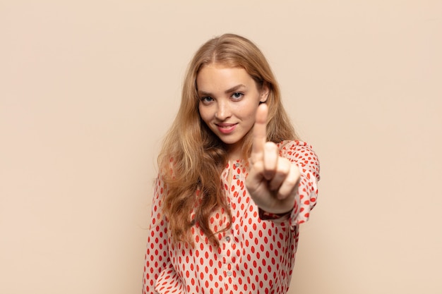 Photo blonde woman smiling proudly and confidently making number one pose triumphantly, feeling like a leader