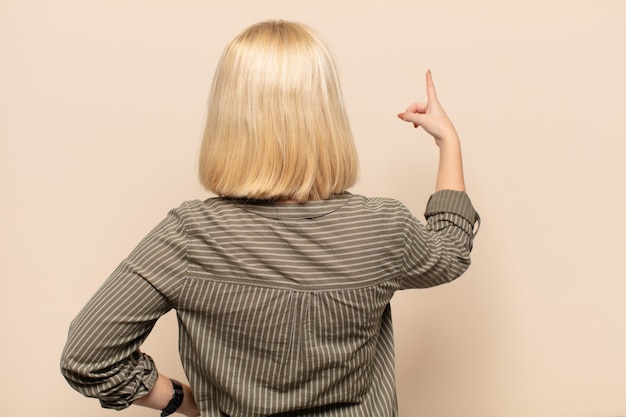 Photo blonde woman standing and pointing to object on copy space, rear view