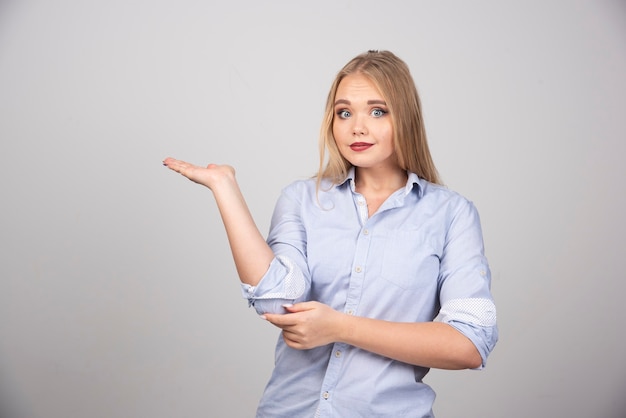 Blonde woman standing and showing opened palm against gray wall .