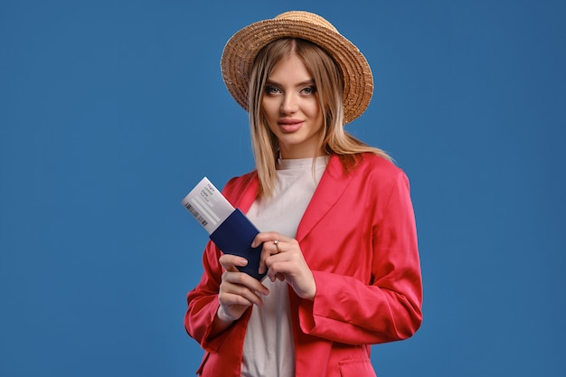 Blonde woman in straw hat holding passport and ticket. Travel concept