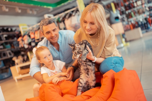 Blonde woman taking grey cat while buying it for her daughter