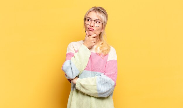 Blonde woman thinking, feeling doubtful and confused, with different options, wondering which decision to make