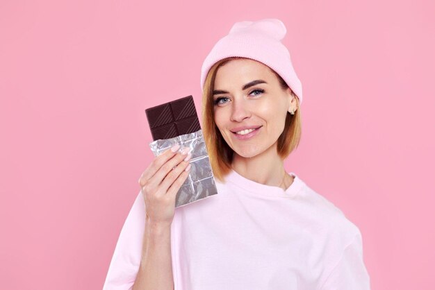 Blonde woman in tshirt and hat holding chocolate bar