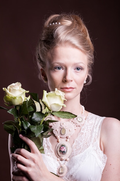 Blonde woman in victorian dress with roses in hands. Rich and vintage. Luxury and elegance. Studio photo