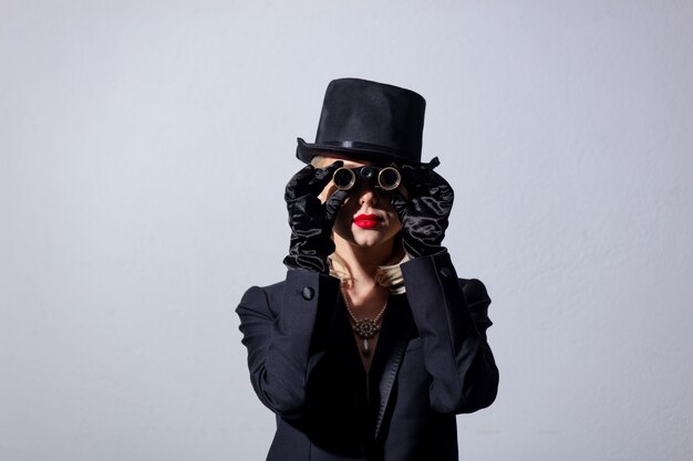 Foto donna bionda in giacca nera vintage e cappello a cilindro con occhiali da opera