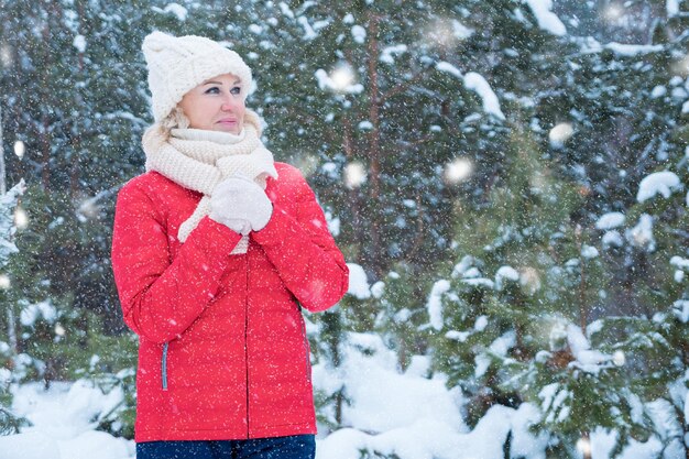 暖かい服を着た金髪の女性が雪の冬の森に立っています