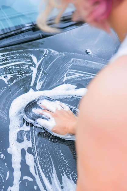 金髪の女性が車のリアビューのボンネットを洗う