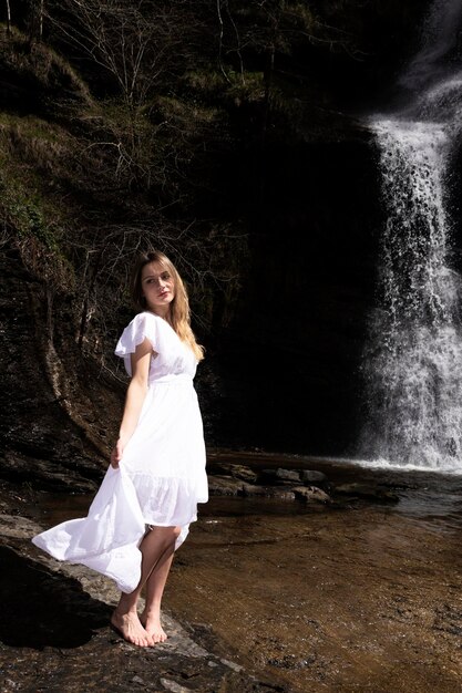 Foto donna bionda in una cascata con un vestito bianco che guarda la telecamera