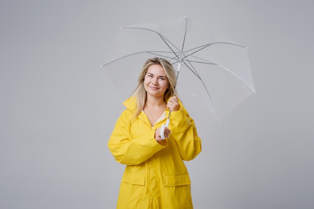 Blonde woman wearing yellow raincoat holding transparent umbrella checking weather if it is raining	