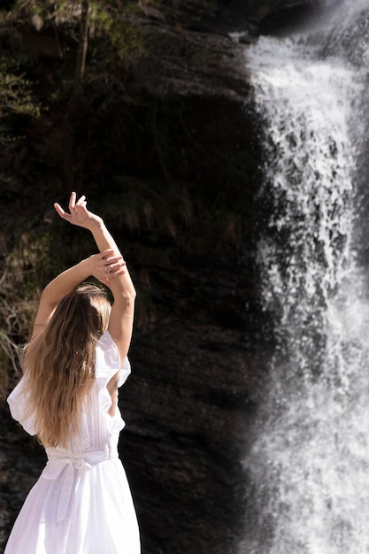 Foto donna bionda con un vestito bianco che guarda una cascata