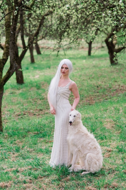 Blonde woman in white dress playing with her russian wolfhound dog in garden