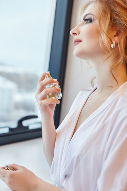 Blonde woman in a white silk robe splashes perfume